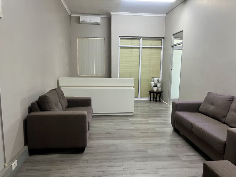 A professional office reception area featuring a built-in desk, wall-mounted air conditioning, modern laminate flooring, and neutral wall finishes.
