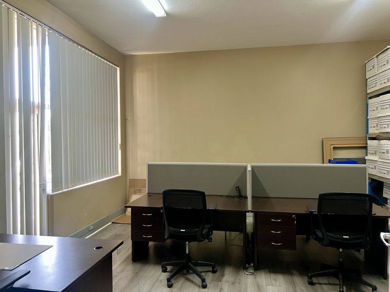 A functional office space featuring laminate flooring, vertical window blinds, and overhead fluorescent lighting, suitable for a professional work environment.