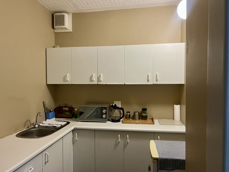 A compact office kitchenette featuring white built-in cabinetry, a stainless steel sink, and a laminate countertop, providing essential utility space for staff.
