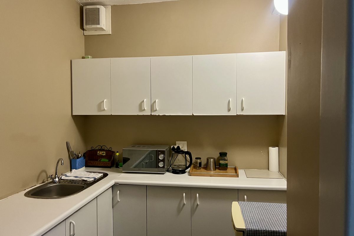 A compact office kitchenette featuring white built-in cabinetry, a stainless steel sink, and a laminate countertop, providing essential utility space for staff.