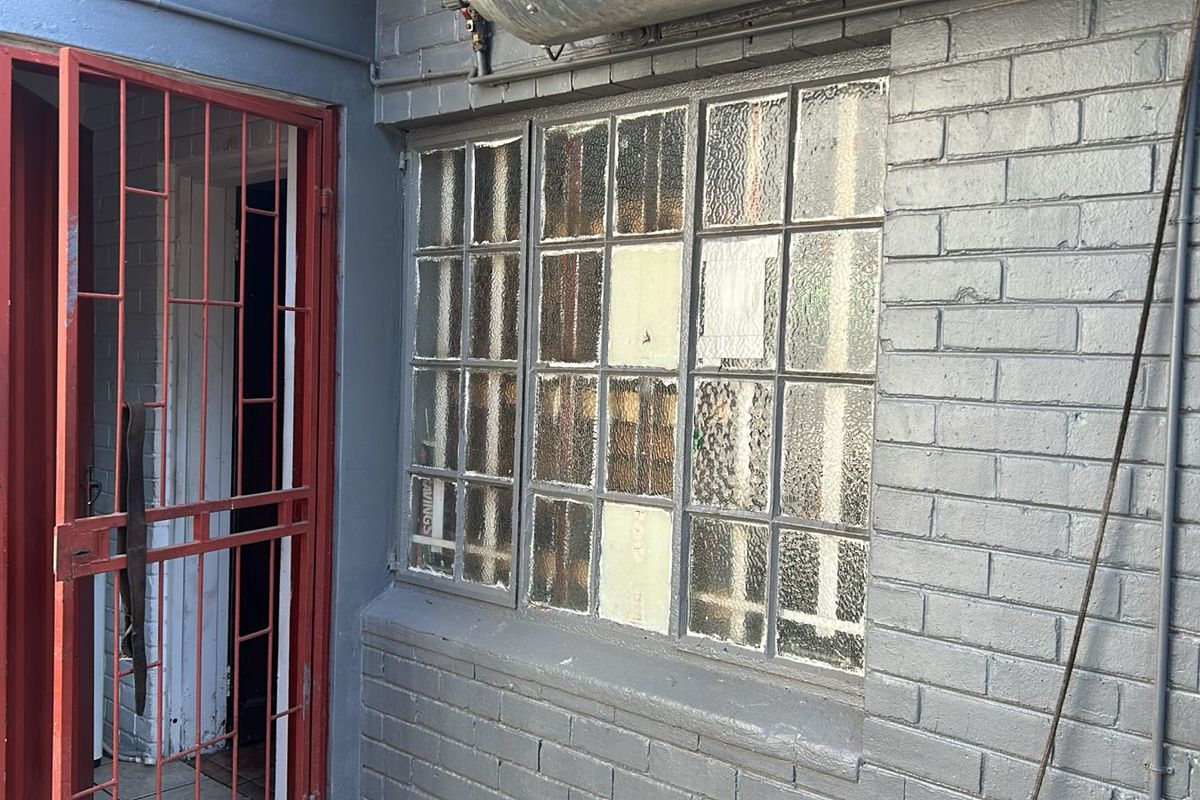 Exterior view of a commercial building featuring a painted brick facade, a red metal security gate, and multi-pane textured glass windows.
