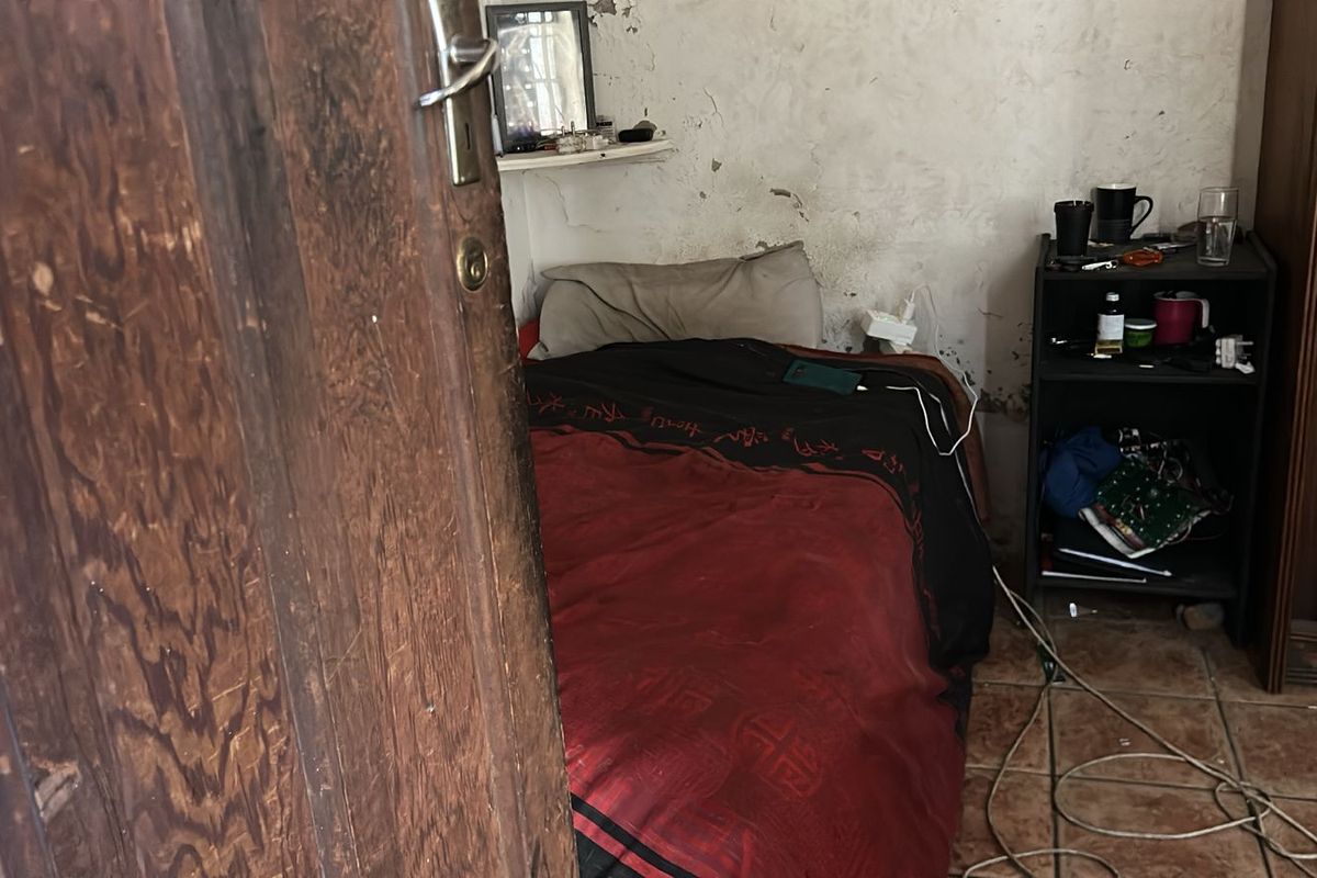 A bedroom interior featuring tiled flooring and walls showing significant signs of wear and surface damage.