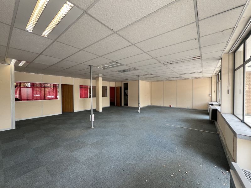 Spacious open-plan office area featuring modular partition walls, suspended ceilings with recessed lighting, and large windows providing ample natural light.