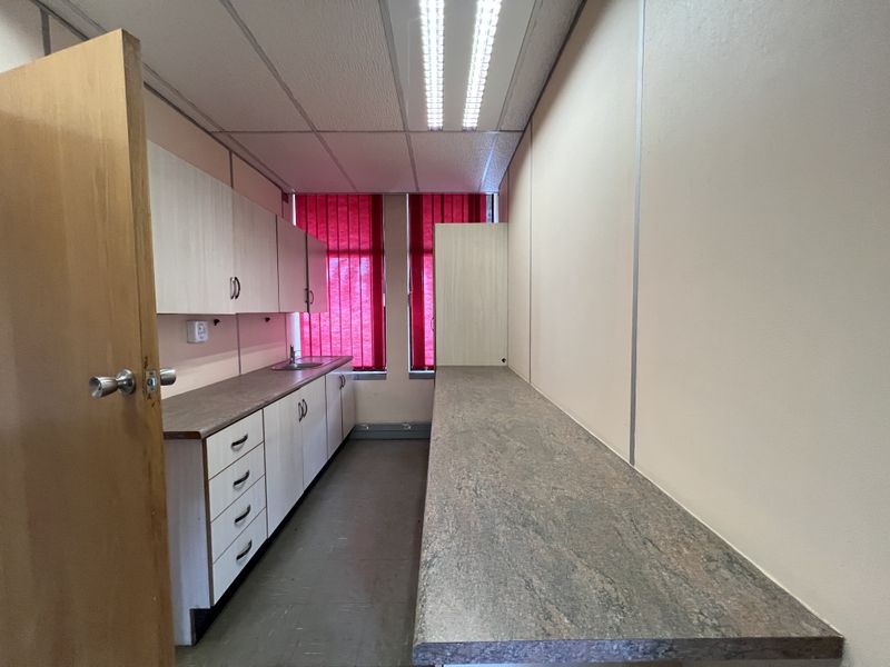 A functional office kitchenette featuring built-in cabinetry, laminate countertops, a stainless steel sink, and drop ceiling lighting.
