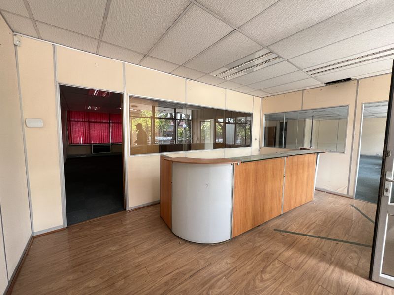 An empty office space featuring a built-in reception desk, glass partitions, and suspended ceiling tiles, suitable for a professional workspace renovation.