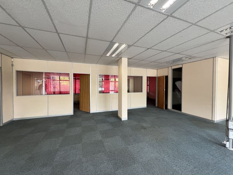 An open-plan office space featuring modular partition walls, internal glass windows, suspended ceilings with recessed lighting, and grey carpet tiles.