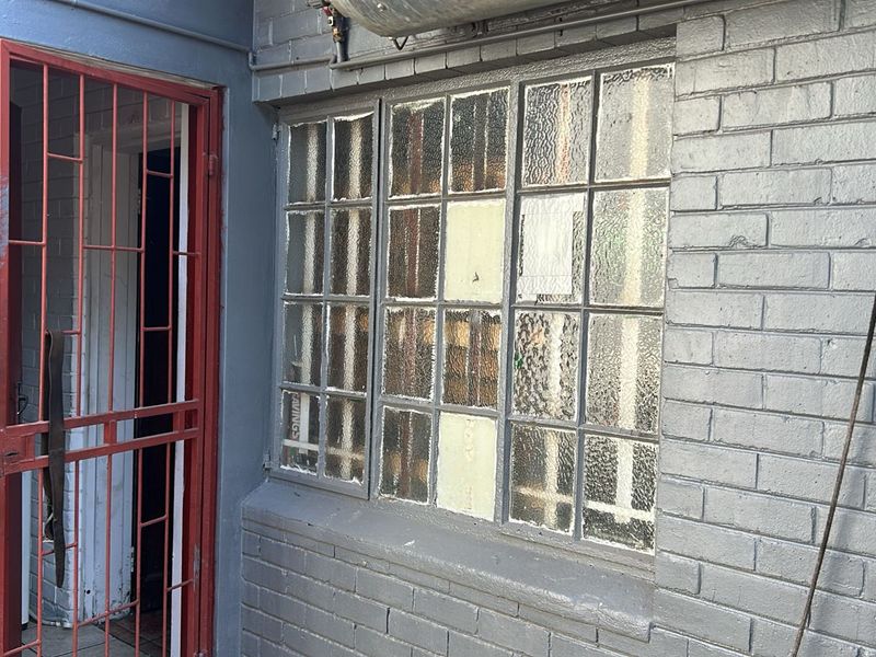 Exterior view of a commercial building featuring a painted brick facade, a red metal security gate, and multi-pane textured glass windows.