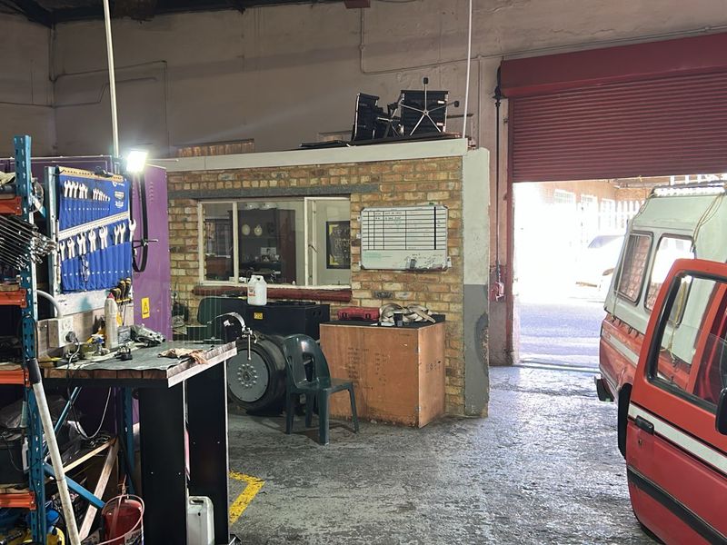Commercial workshop space featuring a roller shutter door, exposed brick office partition, and industrial concrete flooring, suitable for automotive or light industrial use.