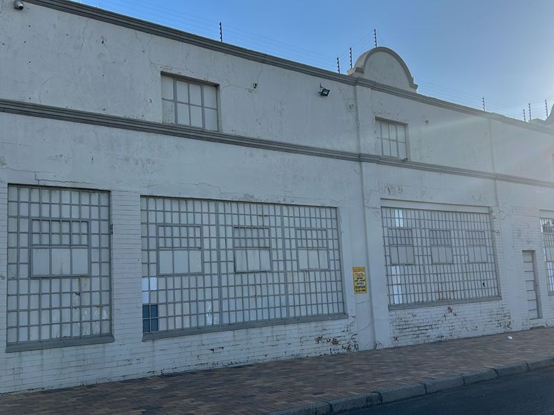 Commercial street-facing facade featuring industrial-style grid windows, security fencing, and a paved sidewalk approach.