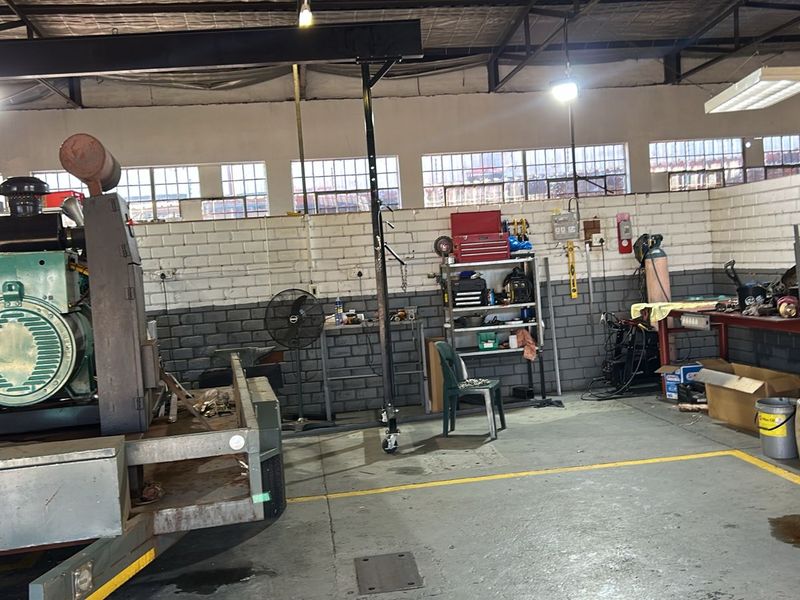 A functional commercial workshop space featuring exposed industrial ceiling, painted brick walls, and concrete flooring, suitable for automotive or mechanical repair operations.