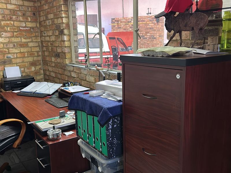 A functional office space featuring exposed brick walls, large windows providing natural light, and practical built-in workspace layout.