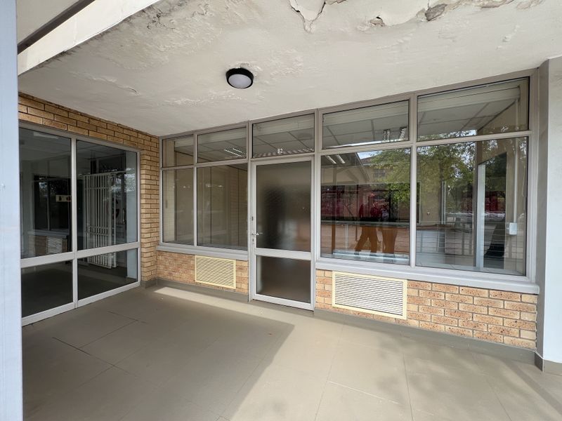 Office entrance area featuring a brick facade, aluminium-framed glass doors and windows, and tiled flooring, showing signs of ceiling damage.