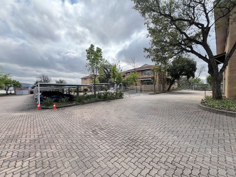 Exterior view of the office property featuring a paved driveway, covered parking carports, and established landscaping around the brick building.
