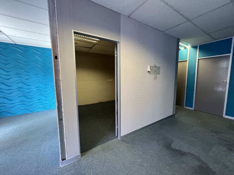 An empty office space featuring suspended ceilings, carpeted flooring, and decorative wall panels, currently showing signs of wear and unfinished wall sections.
