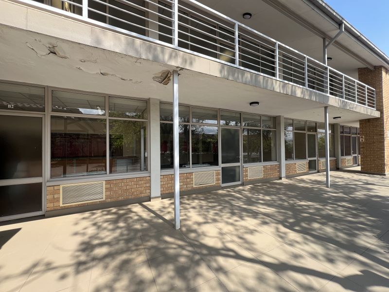 Exterior view of an office building featuring a tiled patio, brick facade, and a balcony with metal railings, showing signs of exterior maintenance needs.