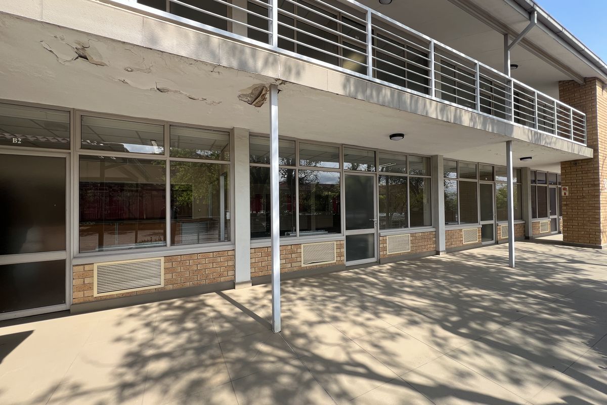 Exterior view of an office building featuring a tiled patio, brick facade, and a balcony with metal railings, showing signs of exterior maintenance needs.
