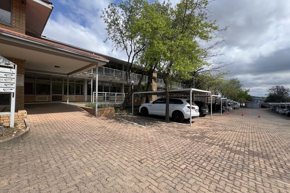 Exterior view of an office building featuring a brick-paved parking area with covered bays and a covered entrance walkway.