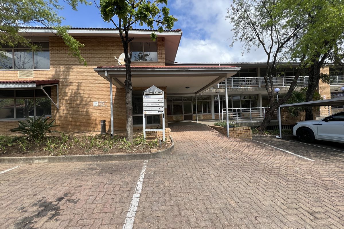 Front exterior view of a brick office building featuring a covered entrance, paved parking area, and directional signage.