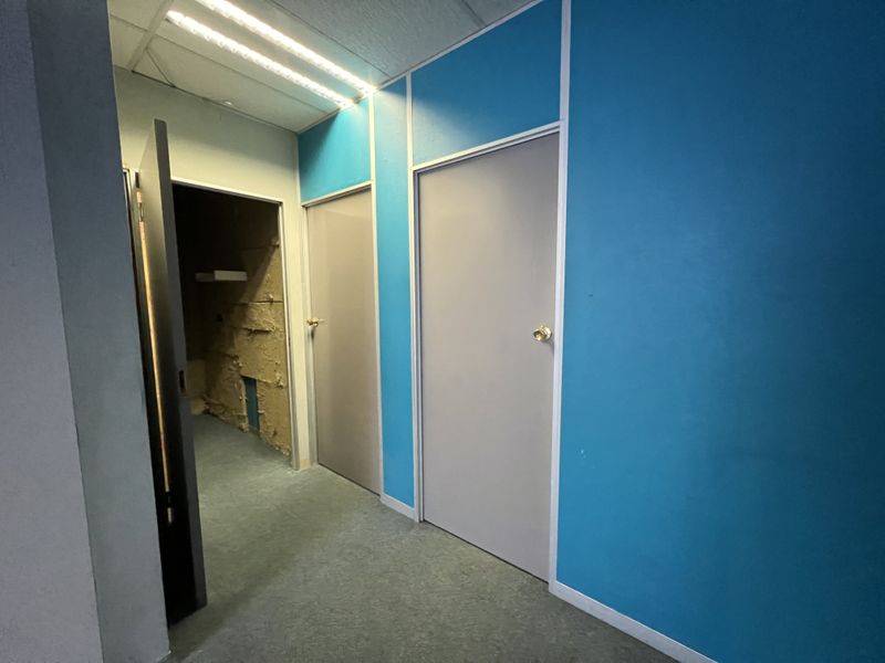 A commercial office hallway featuring partition walls, internal doors, and a suspended ceiling, currently showing signs of unfinished construction or maintenance work.