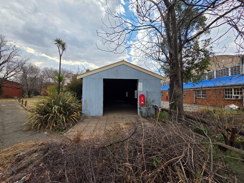 A detached corrugated metal utility structure or garage building situated on a neglected site with overgrown landscaping and visible exterior wear.