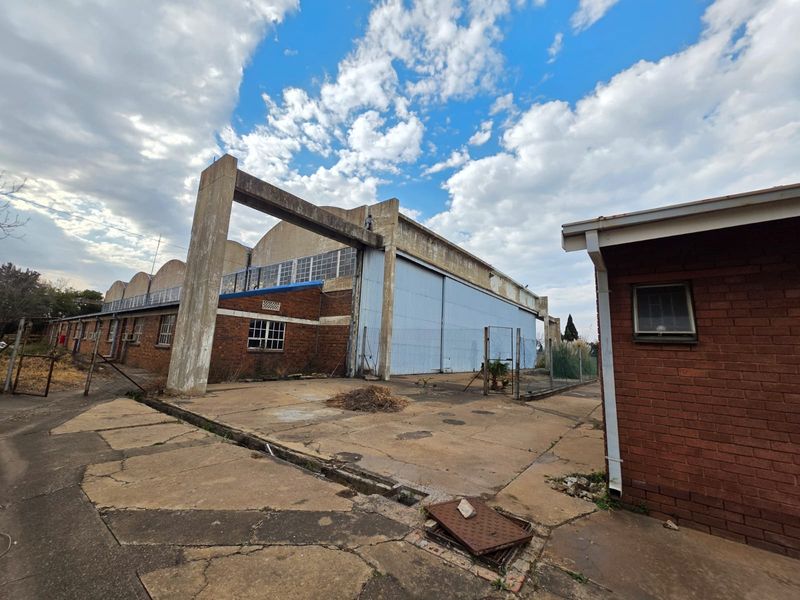 Exterior view of a large industrial hangar facility featuring brick construction, expansive sliding metal doors, and surrounding concrete yard space in need of maintenance.