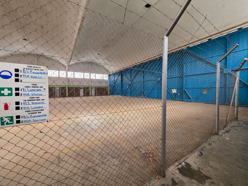 Large industrial warehouse or hangar space featuring high vaulted ceilings, concrete flooring, and secure chain-link partitioning.