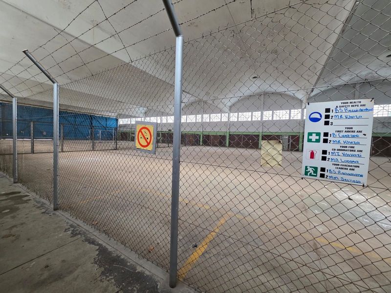 Large industrial or warehouse space featuring high vaulted ceilings, concrete flooring, and secure chain-link perimeter fencing.