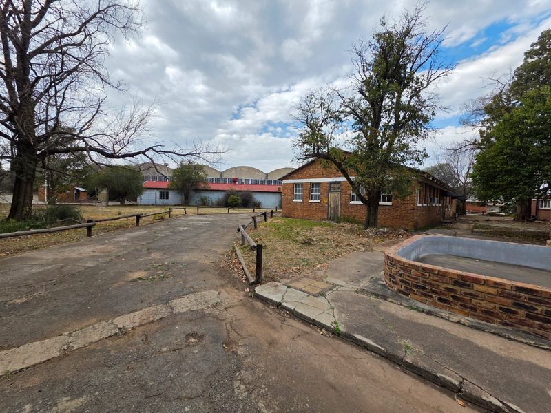 Exterior view of a commercial property featuring brick buildings, paved driveway, and a small circular brick structure on a large plot.