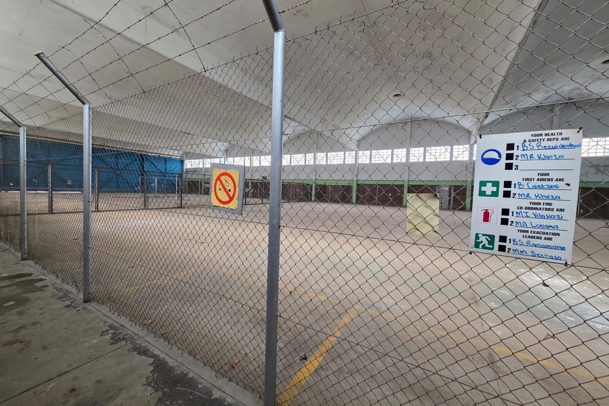 Large industrial or warehouse space featuring high vaulted ceilings, concrete flooring, and secure chain-link perimeter fencing.