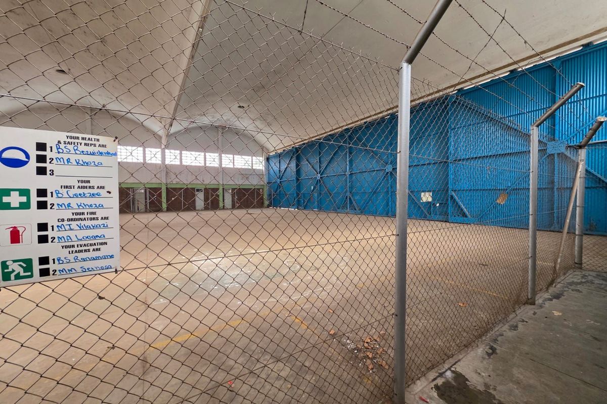 Large industrial warehouse or hangar space featuring high vaulted ceilings, concrete flooring, and secure chain-link partitioning.