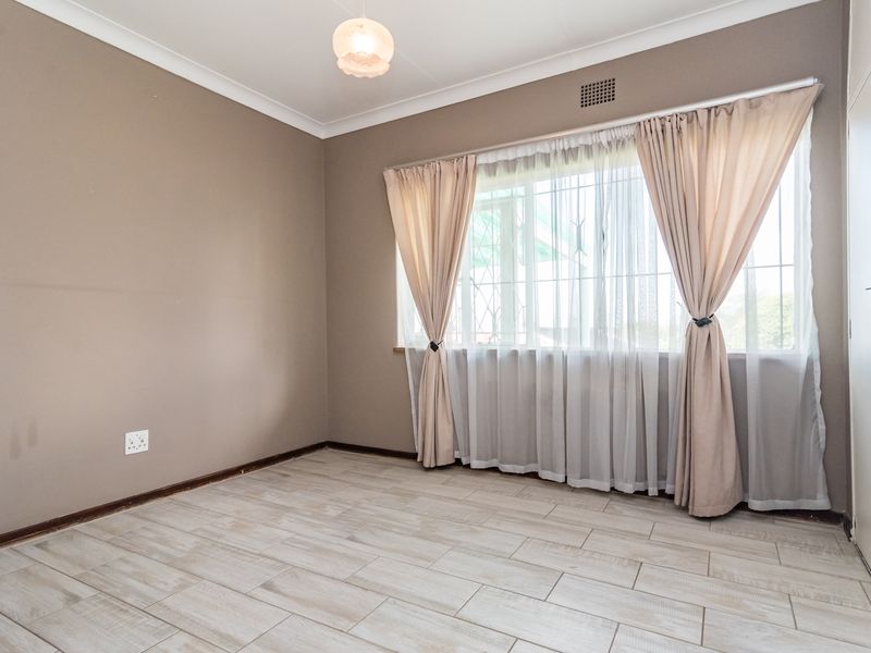 A vacant bedroom featuring light-toned tiled flooring, neutral wall paint, security bars on the window, and a built-in cupboard.