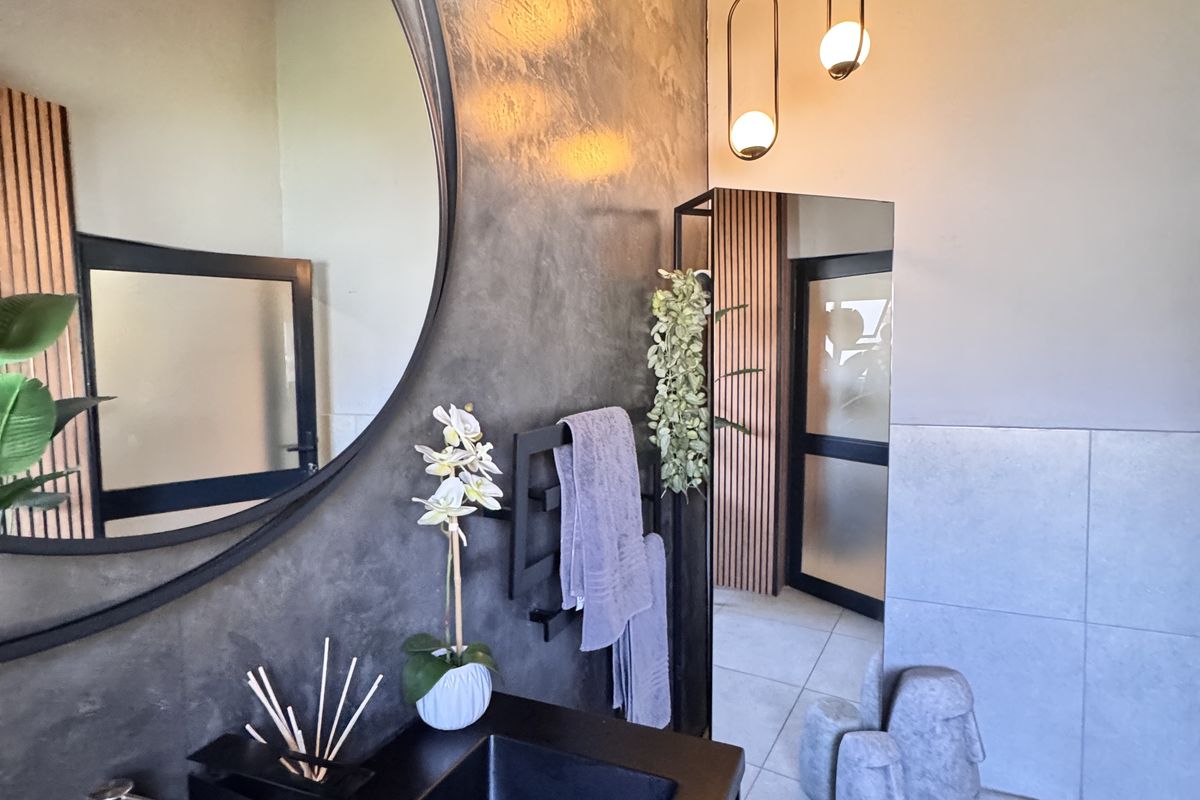 Modern bathroom featuring a sleek black vanity, integrated basin, large circular mirror, and contemporary pendant lighting with textured wall finishes.