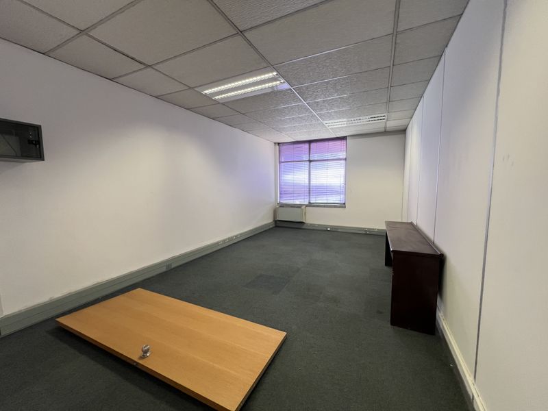 A vacant office space featuring a suspended ceiling, recessed lighting, wall-mounted HVAC unit, and carpeted flooring, suitable for a professional workspace.