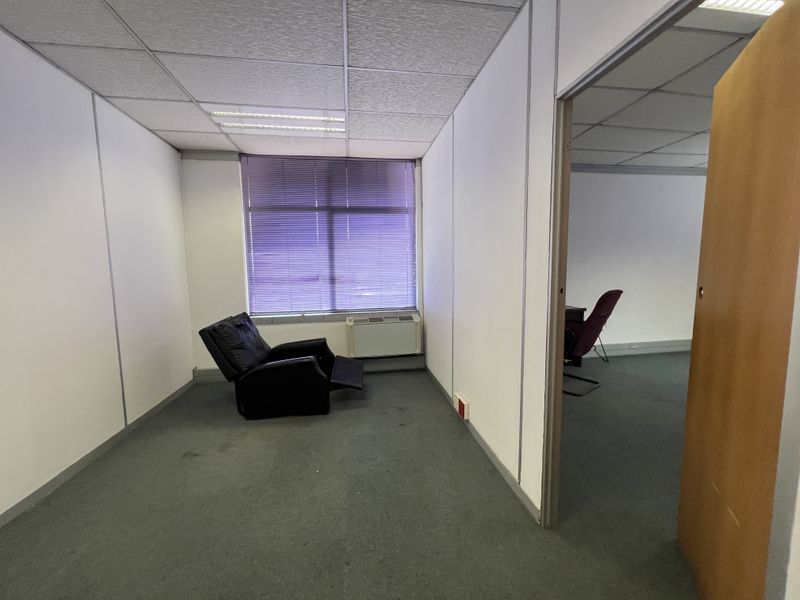 A vacant office space featuring suspended ceilings, recessed lighting, carpeted flooring, and a window with fitted blinds.