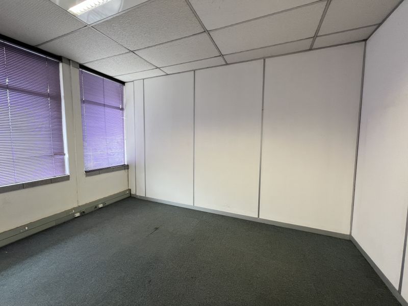 An empty office space featuring modular partition walls, carpet flooring, suspended ceiling with recessed lighting, and venetian blinds.