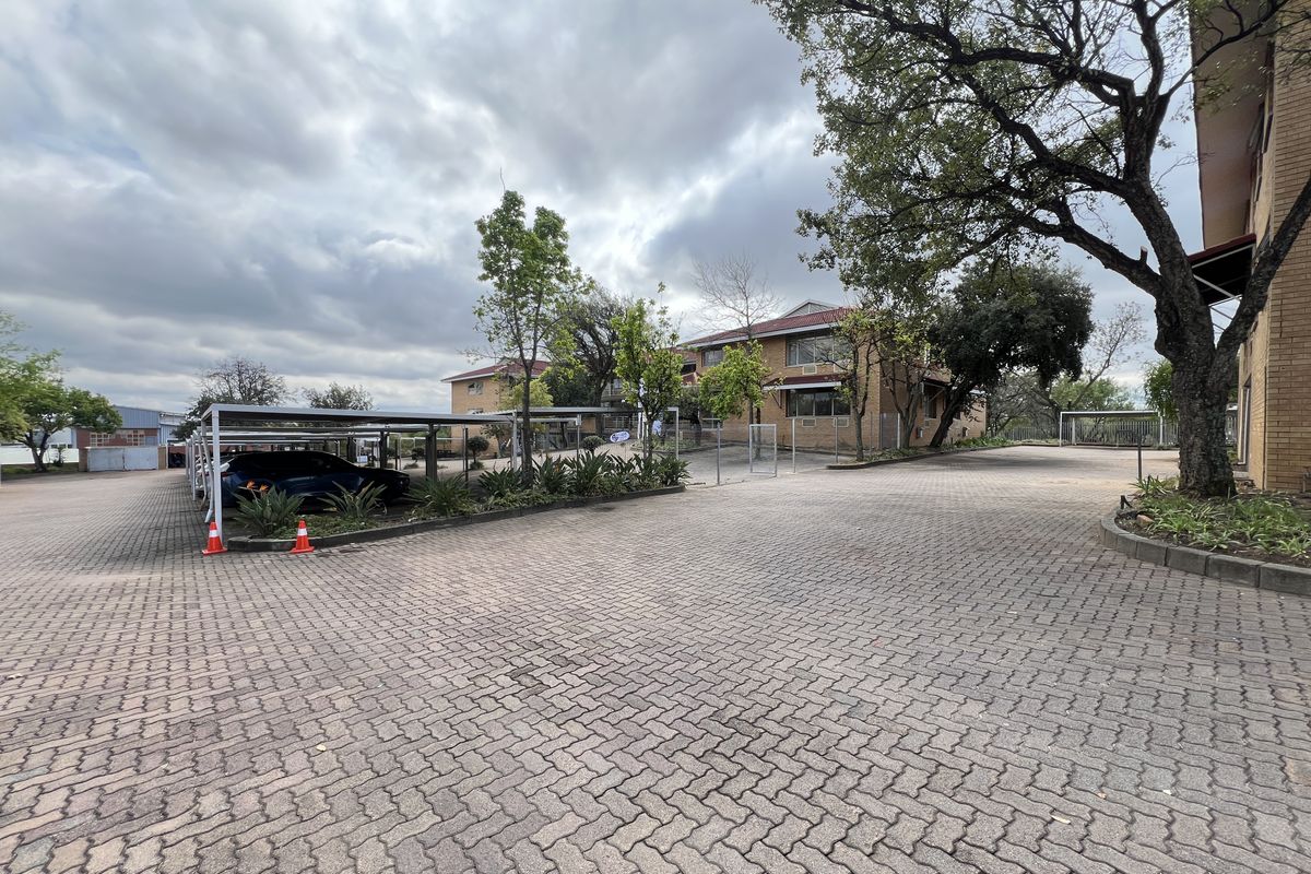 Exterior view of the office property featuring a paved driveway, covered parking carports, and established landscaping around the brick building.