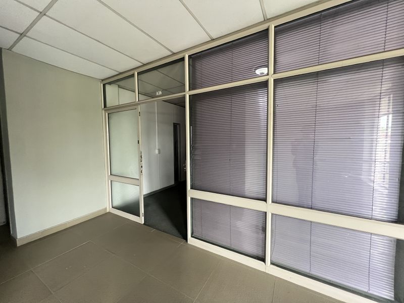 An empty office space featuring aluminium-framed glass partitioning with integrated blinds, a suspended ceiling, and tiled flooring.