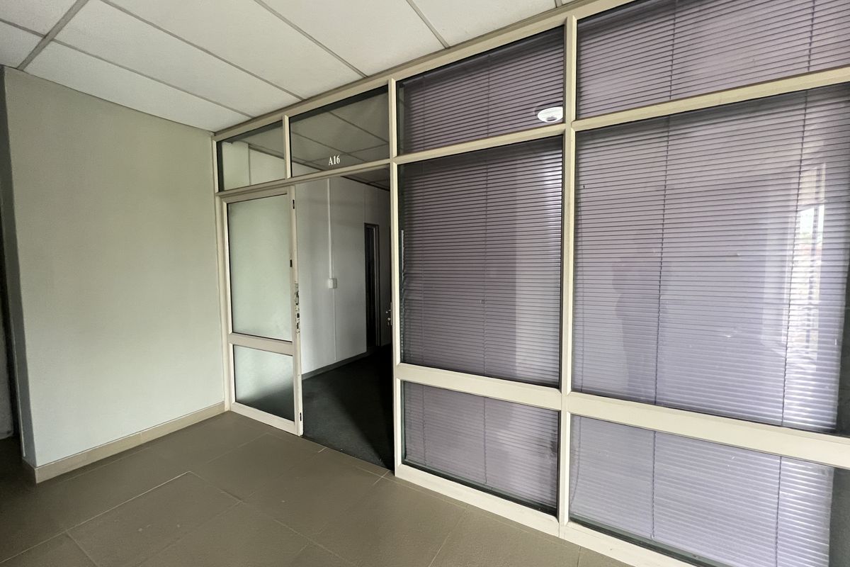 An empty office space featuring aluminium-framed glass partitioning with integrated blinds, a suspended ceiling, and tiled flooring.