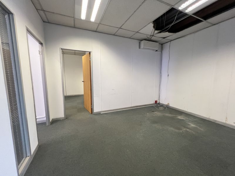An empty office space featuring carpet flooring, a split-system air conditioner, and a suspended ceiling with visible damage and exposed wiring.