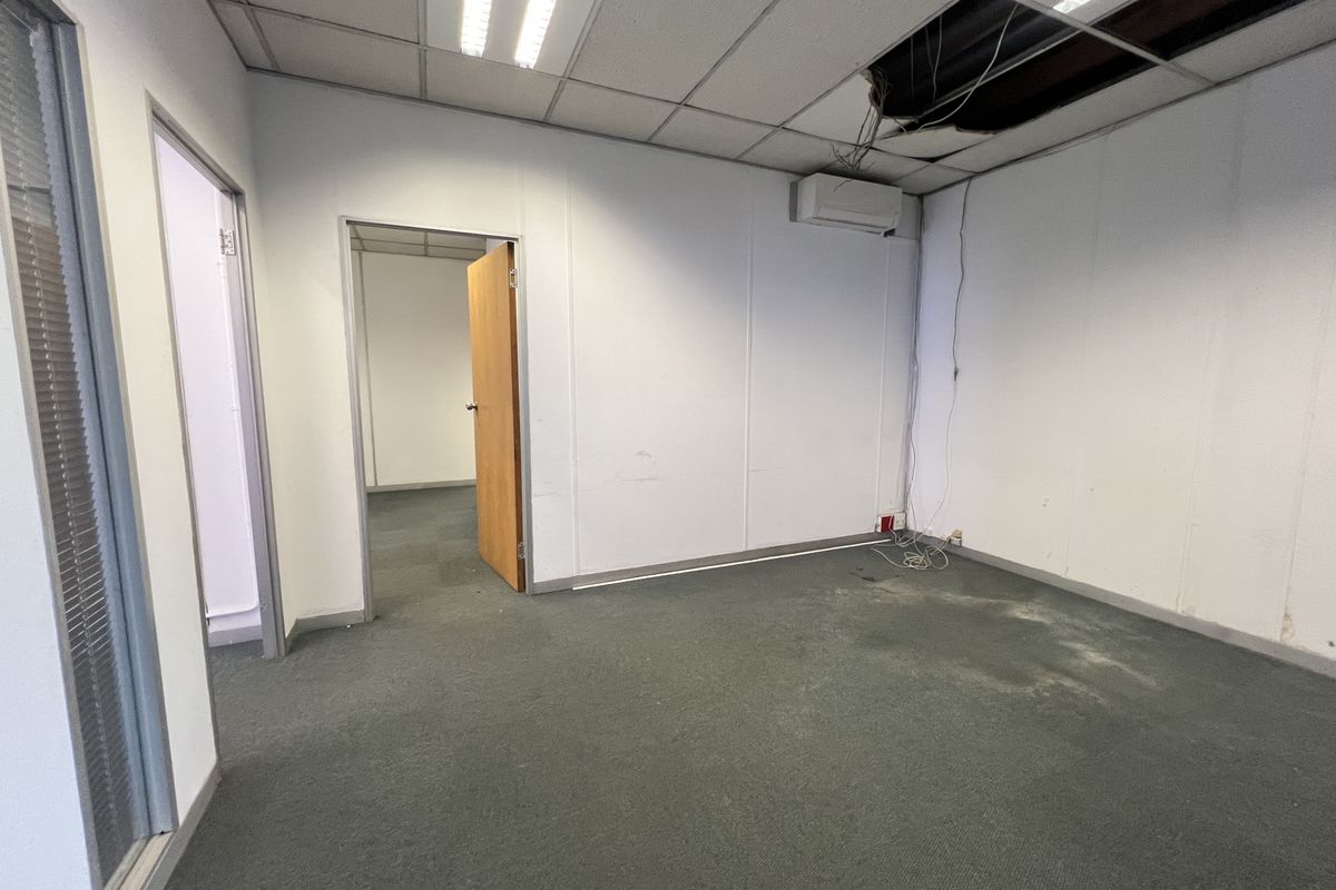 An empty office space featuring carpet flooring, a split-system air conditioner, and a suspended ceiling with visible damage and exposed wiring.