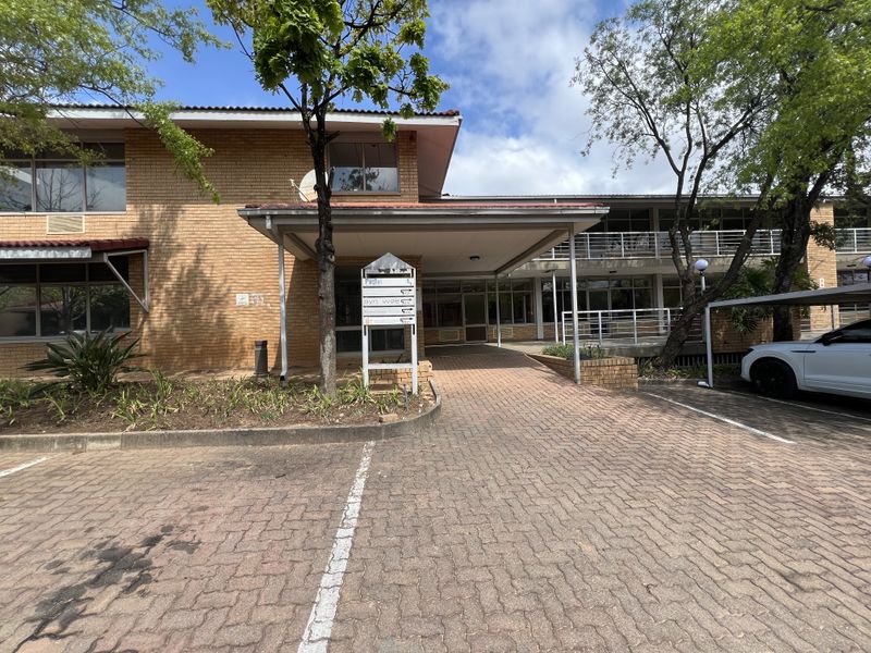 Front exterior view of a brick office building featuring a covered entrance, paved parking area, and directional signage.