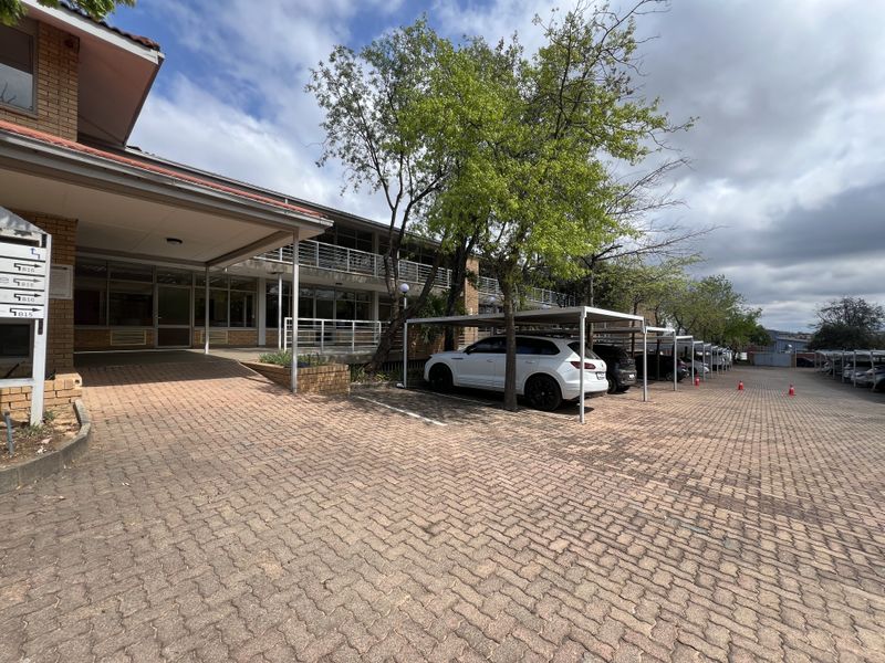 Exterior view of an office building featuring a brick-paved parking area with covered bays and a covered entrance walkway.