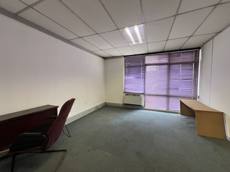 A functional office space featuring a suspended ceiling, recessed lighting, an integrated HVAC unit, and large windows with fitted blinds.