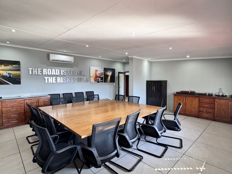 A professional boardroom featuring large wooden conference table, built-in cabinetry, tiled flooring, and wall-mounted air conditioning unit.