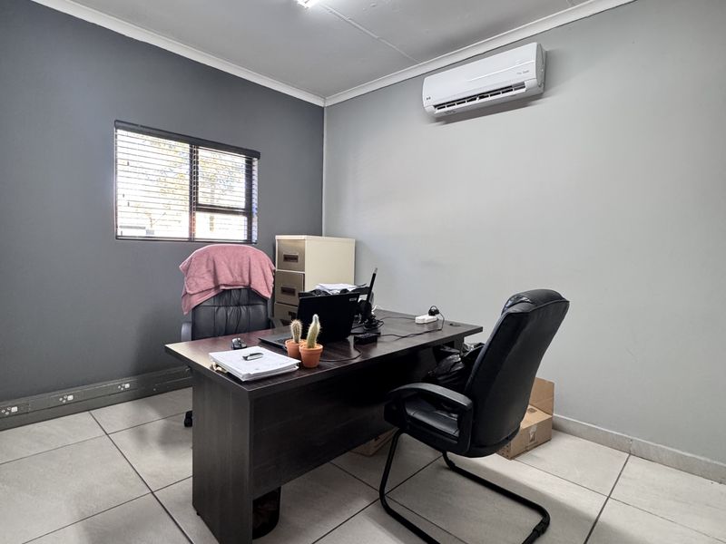 A functional office space featuring tiled flooring, a wall-mounted air conditioning unit, and neutral grey wall finishes.