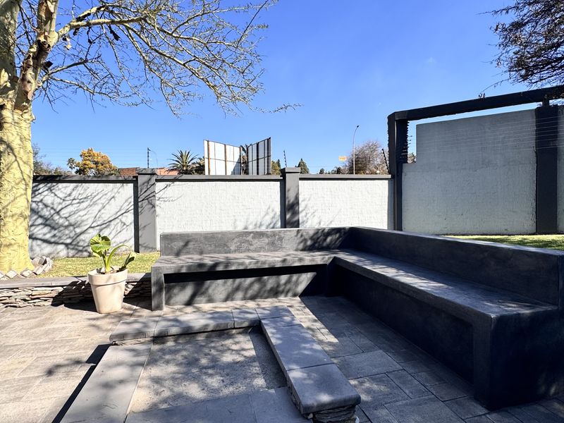 Outdoor entertainment area featuring a built-in concrete bench and a stone-clad fire pit set on a paved patio within a walled garden.