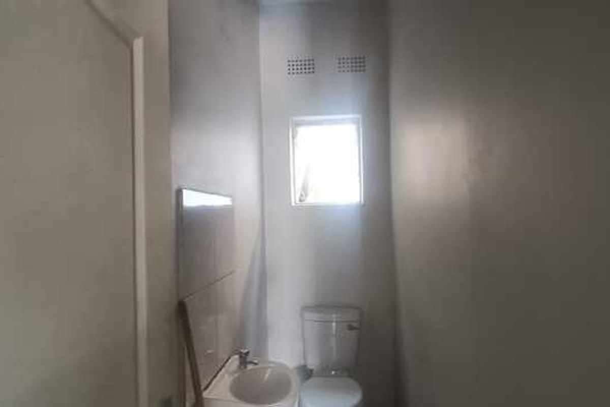 A compact bathroom featuring a standard toilet and a small wall-mounted basin with tiled splashback.