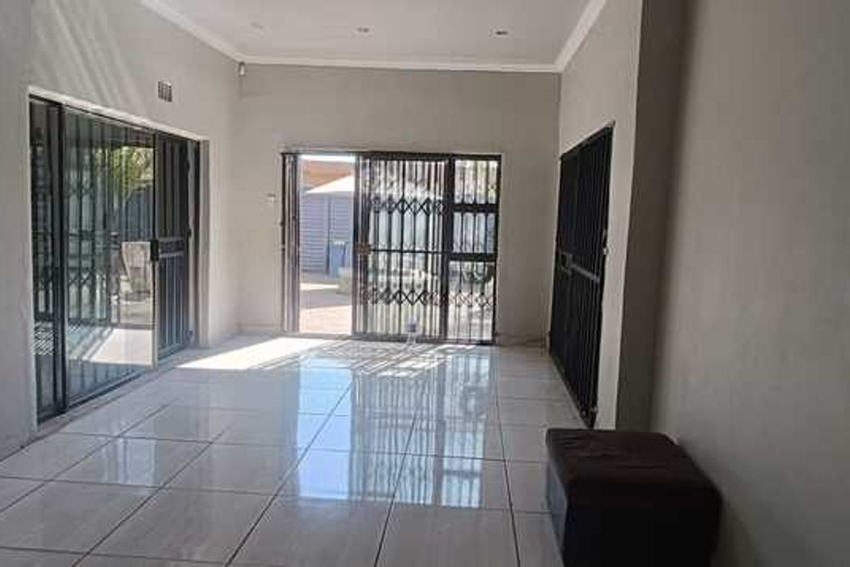 Spacious living area featuring large tiled flooring, recessed ceiling lighting, and multiple sliding glass doors with security gates leading to the exterior.