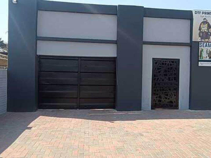 Front exterior view of a commercial property featuring a paved driveway, dark metal security gate, decorative entrance door, and exterior signage.