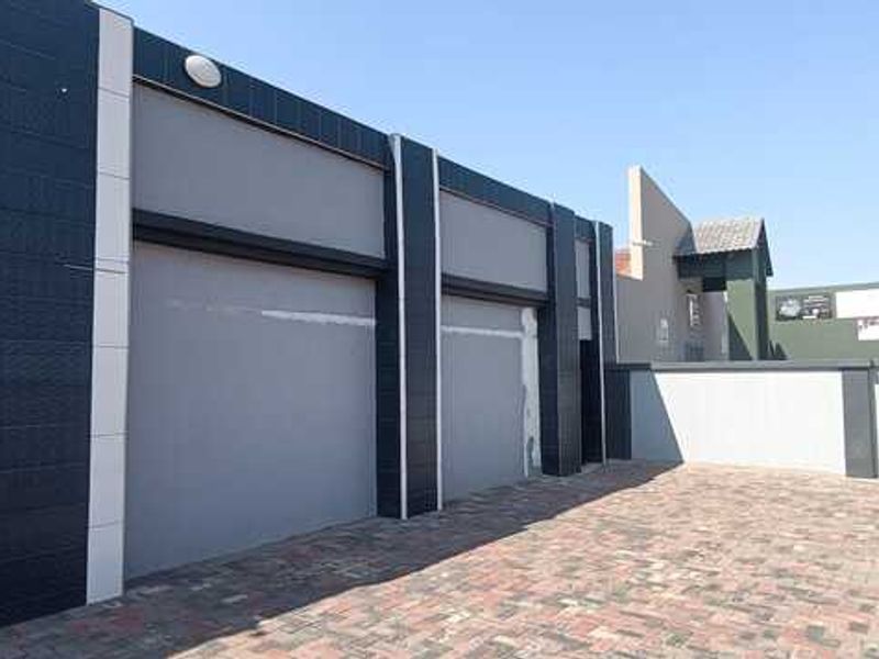 Exterior view of a commercial property featuring a paved courtyard, modern dark-tiled facade, and secure garage-style access points.